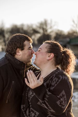 Romantic couple leaning in for a kiss outdoors in winter sunlight, woman placing hands on mans chest.