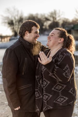 Happy couple laughing together outdoors in winter light, woman in patterned sweater touching mans jacket.