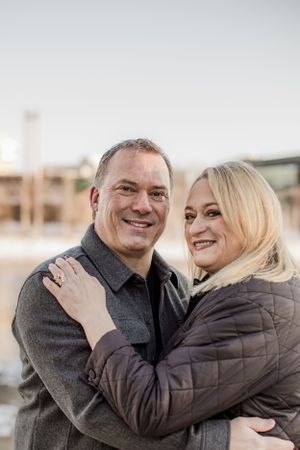 Smiling couple embracing outdoors in winter, woman with blonde hair wearing quilted jacket and diamond ring.