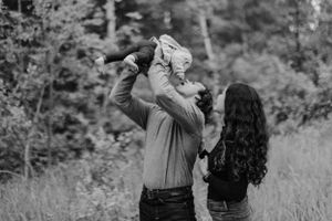 Black and white photo of parents lifting their baby in a natural outdoor setting.