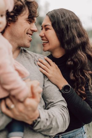 Smiling couple gazing at each other lovingly while holding their baby outdoors.