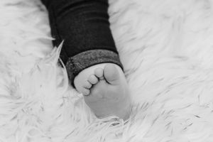 Close-up black and white photo of tiny newborn baby feet on fluffy white fur.