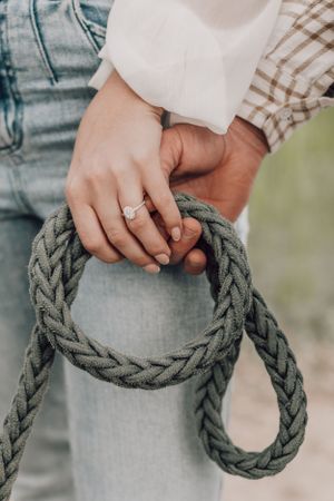 Close-up of an engaged couples hands holding a braided rope, showcasing a diamond ring.