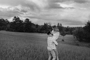 A black and white photo of a couple embracing in a vast open field at dusk.