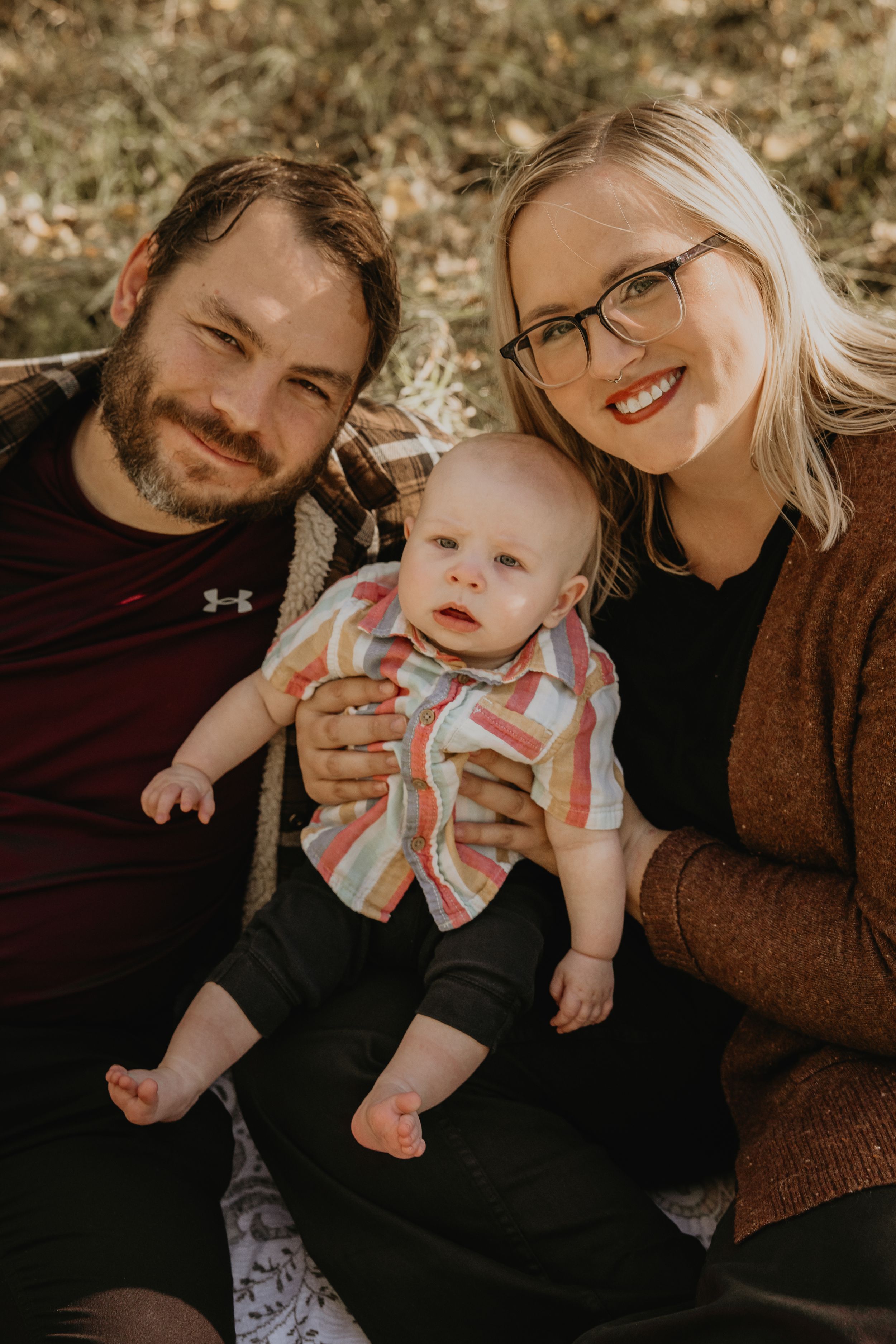 Happy young couple with their smiling baby sitting outdoors in warm autumn natural light.
