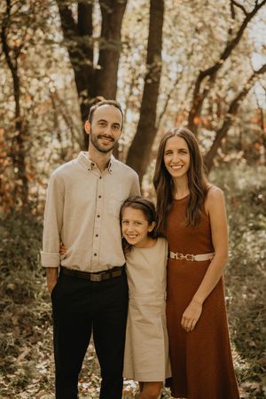 Family of three posing together in an autumn forest setting with warm golden foliage.