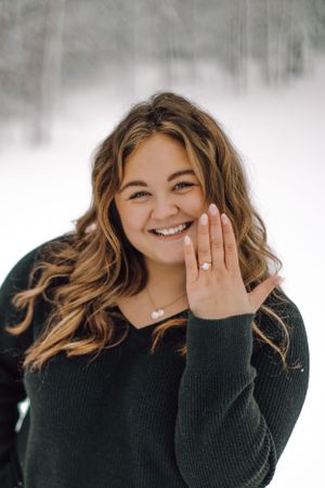 Smiling woman showing off engagement ring in snowy winter outdoor setting.
