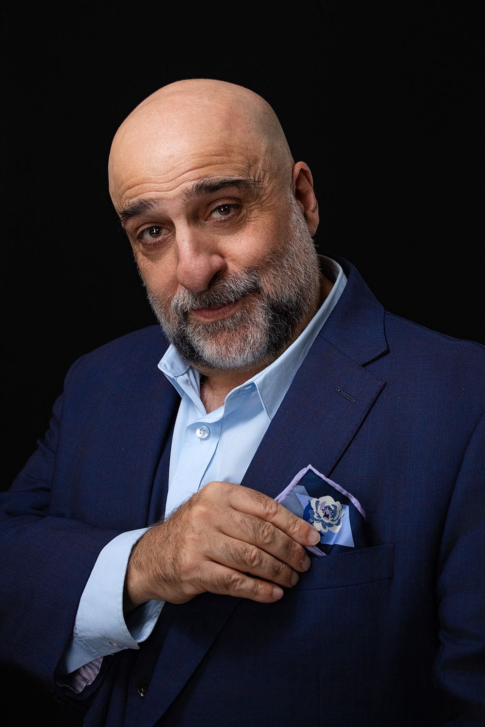 Omid Djalili touching his pocket handkerchief with a funny expression on his face