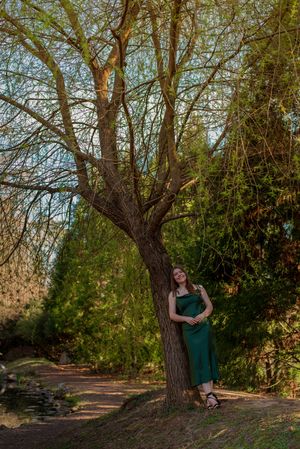 Young woman, smiling against a tree outdoors
