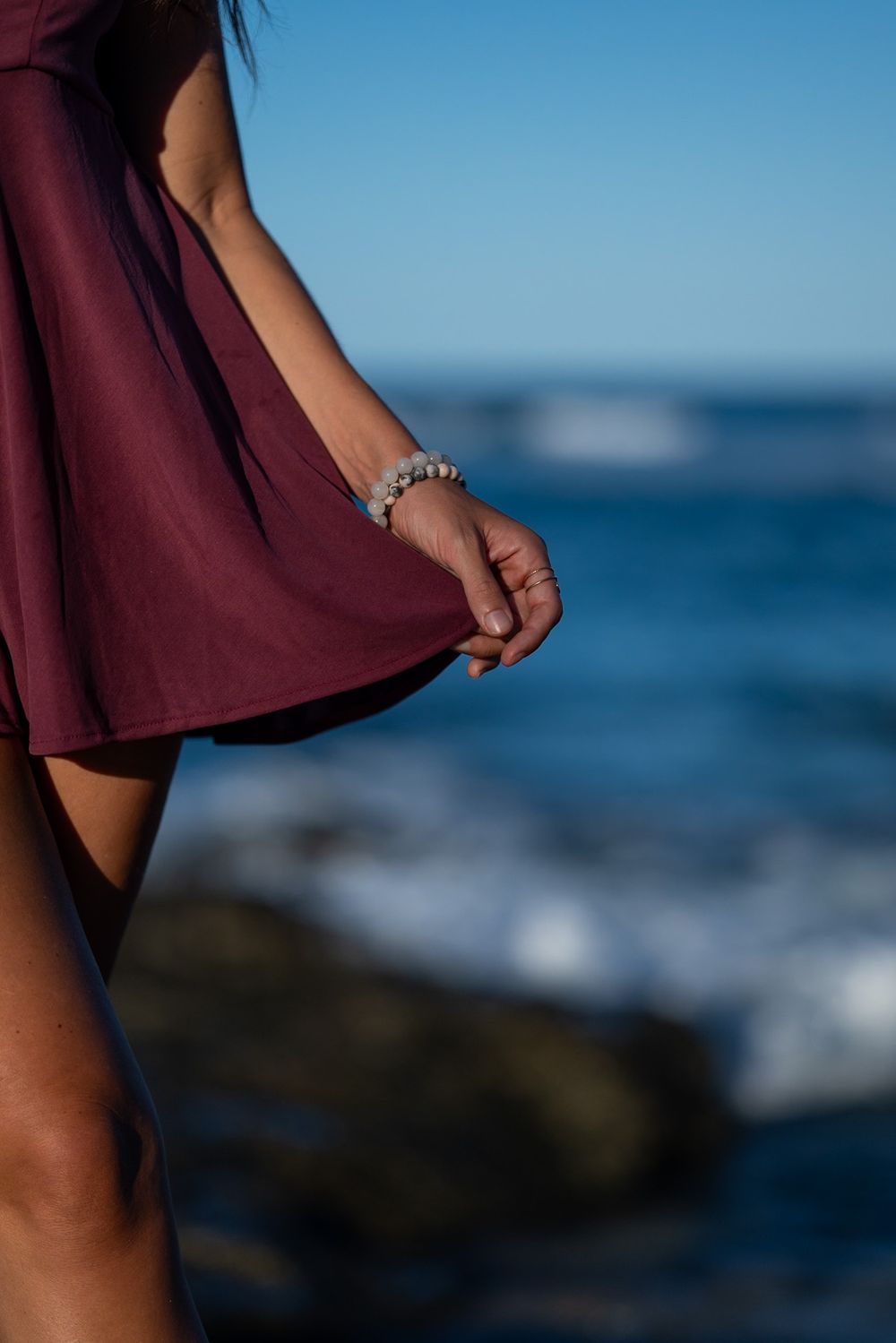 Close-up of flowing burgundy dress with bracelet detail against ocean backdrop.