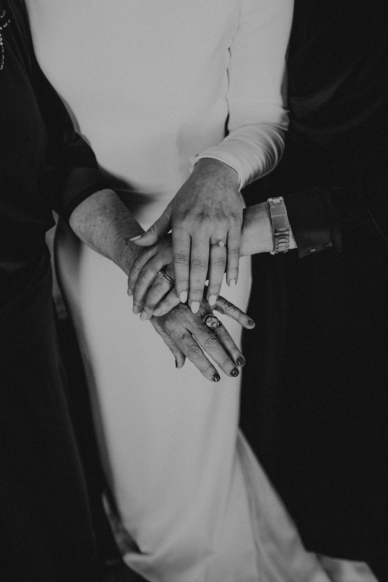 Close-up black and white photo showing clasped hands with engagement rings creating an artistic wedding detail shot.
