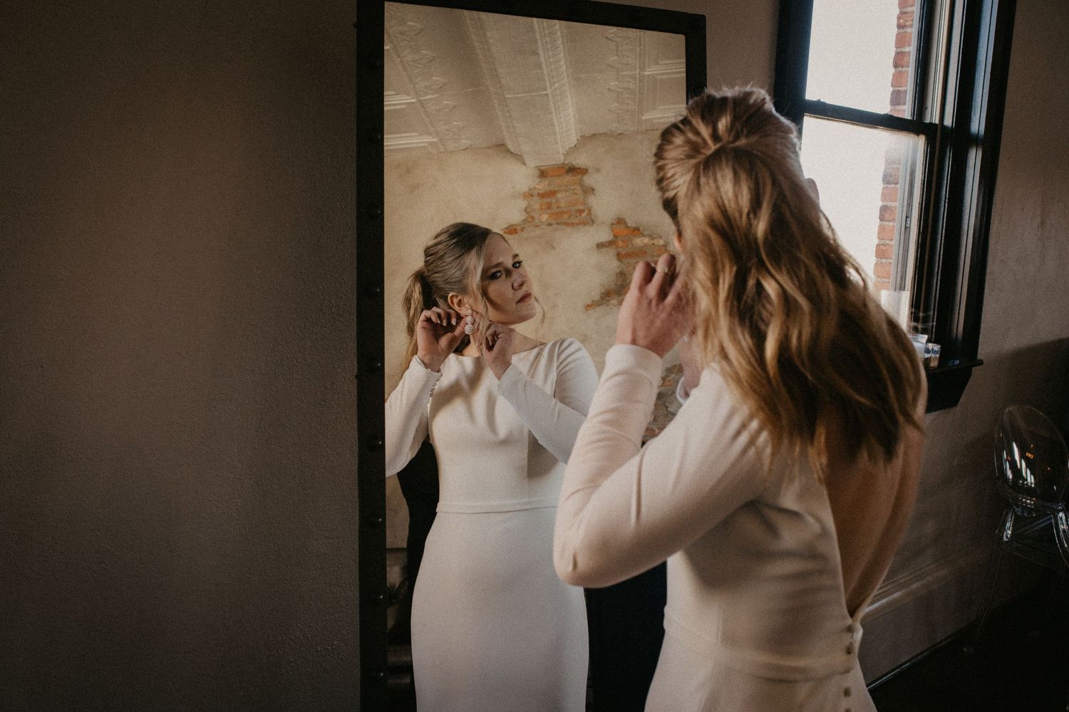 A Bride seen through a mirror wearing a cream-colored sweater in moody, dramatic lighting.