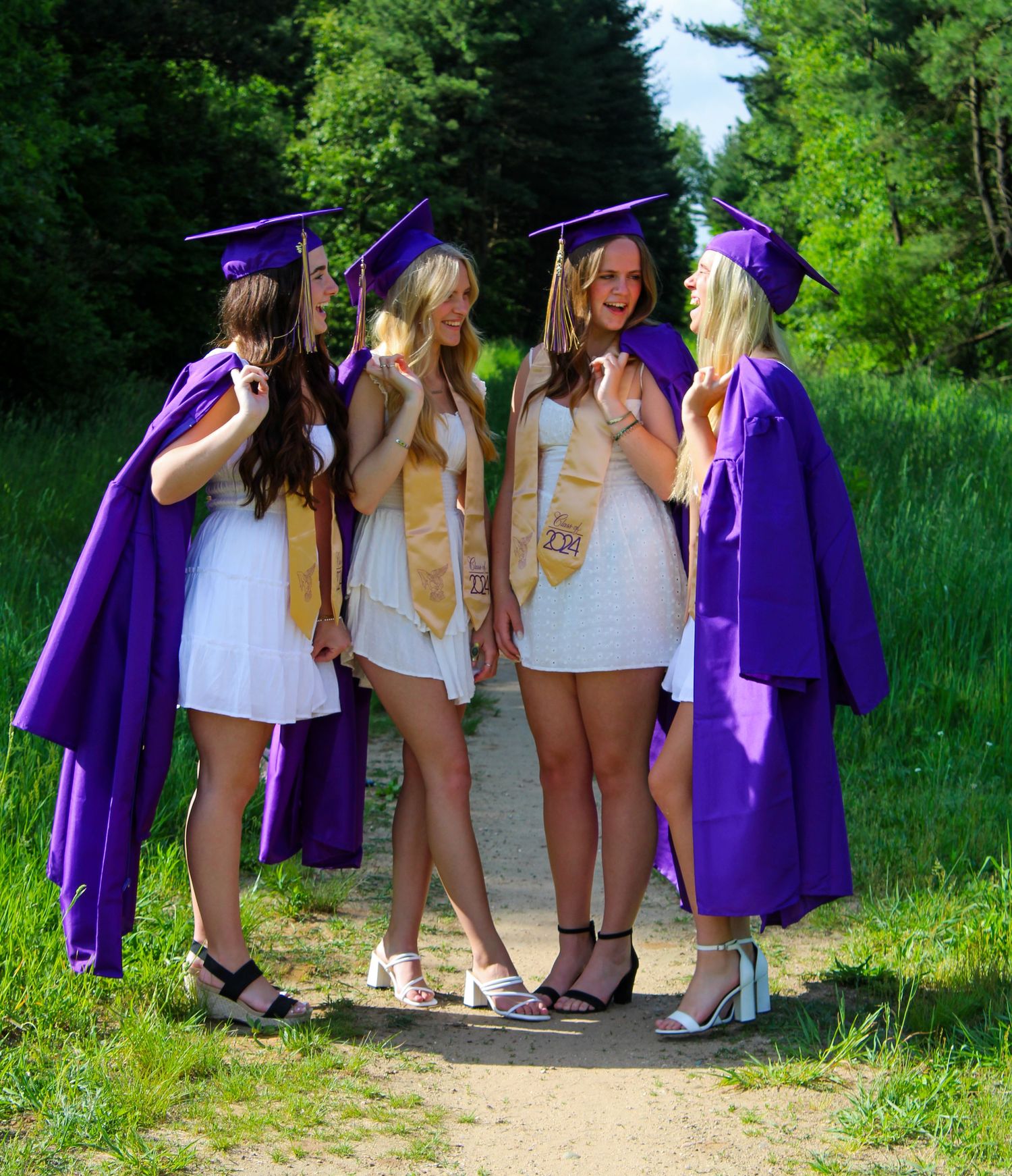 Group wearing purple graduation gowns posing together on a nature path.