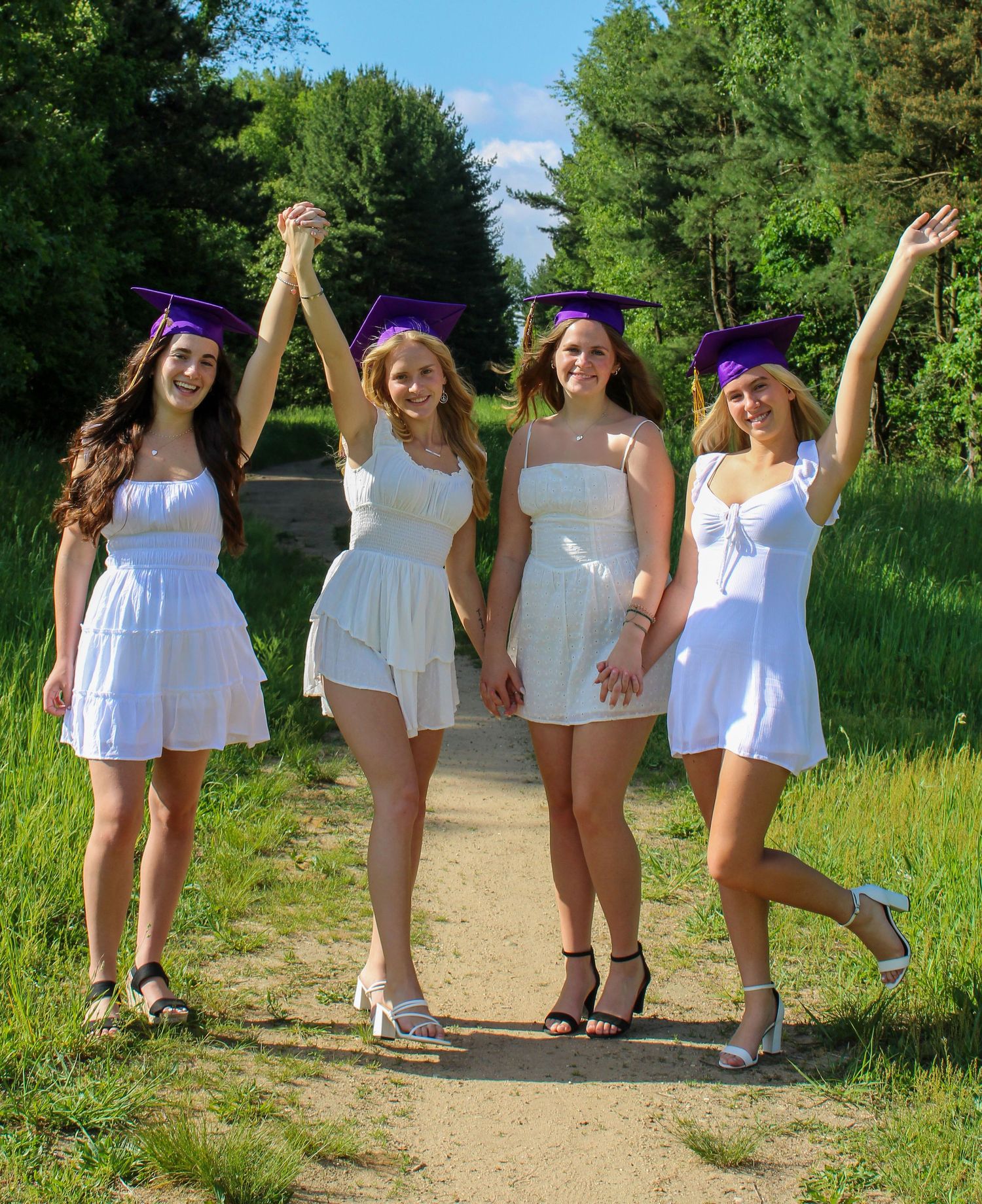 Friends in white outfits celebrating graduation outdoors.
