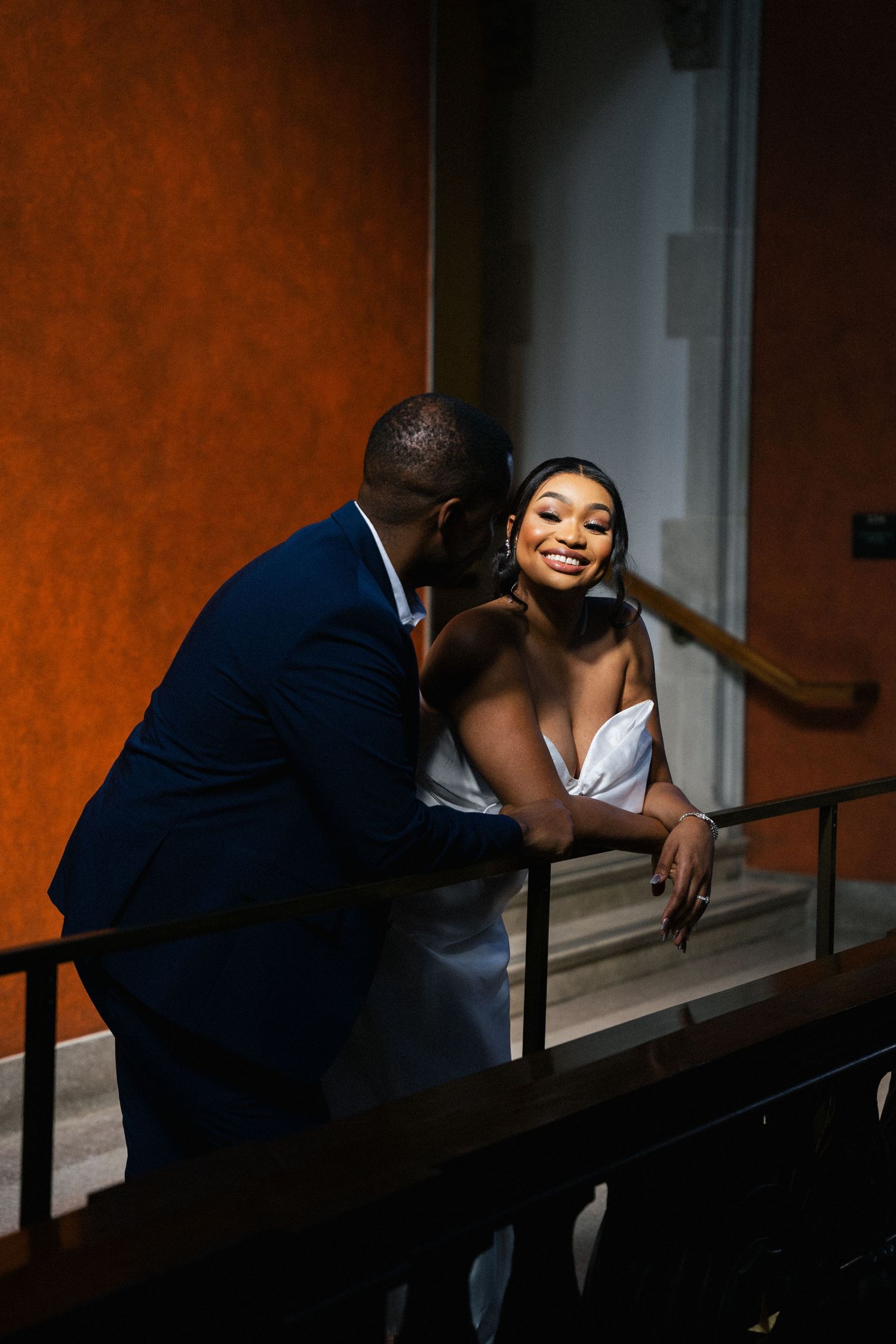 Intimate moment between couple on staircase with warm lighting and formal attire.