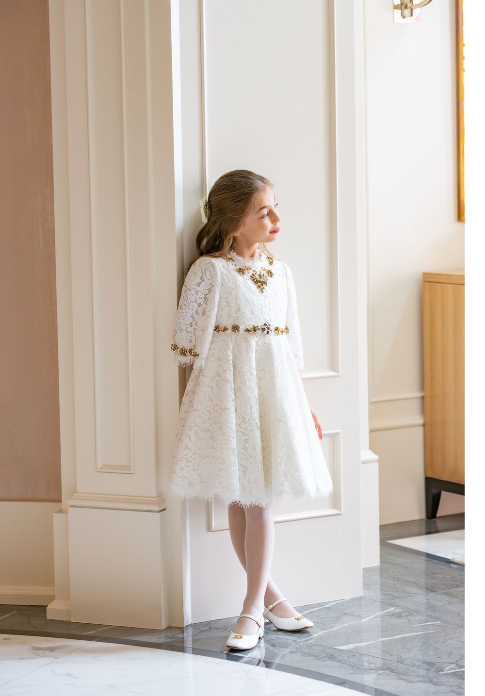 Elegant white lace dress with gold details showcased in refined interior setting.