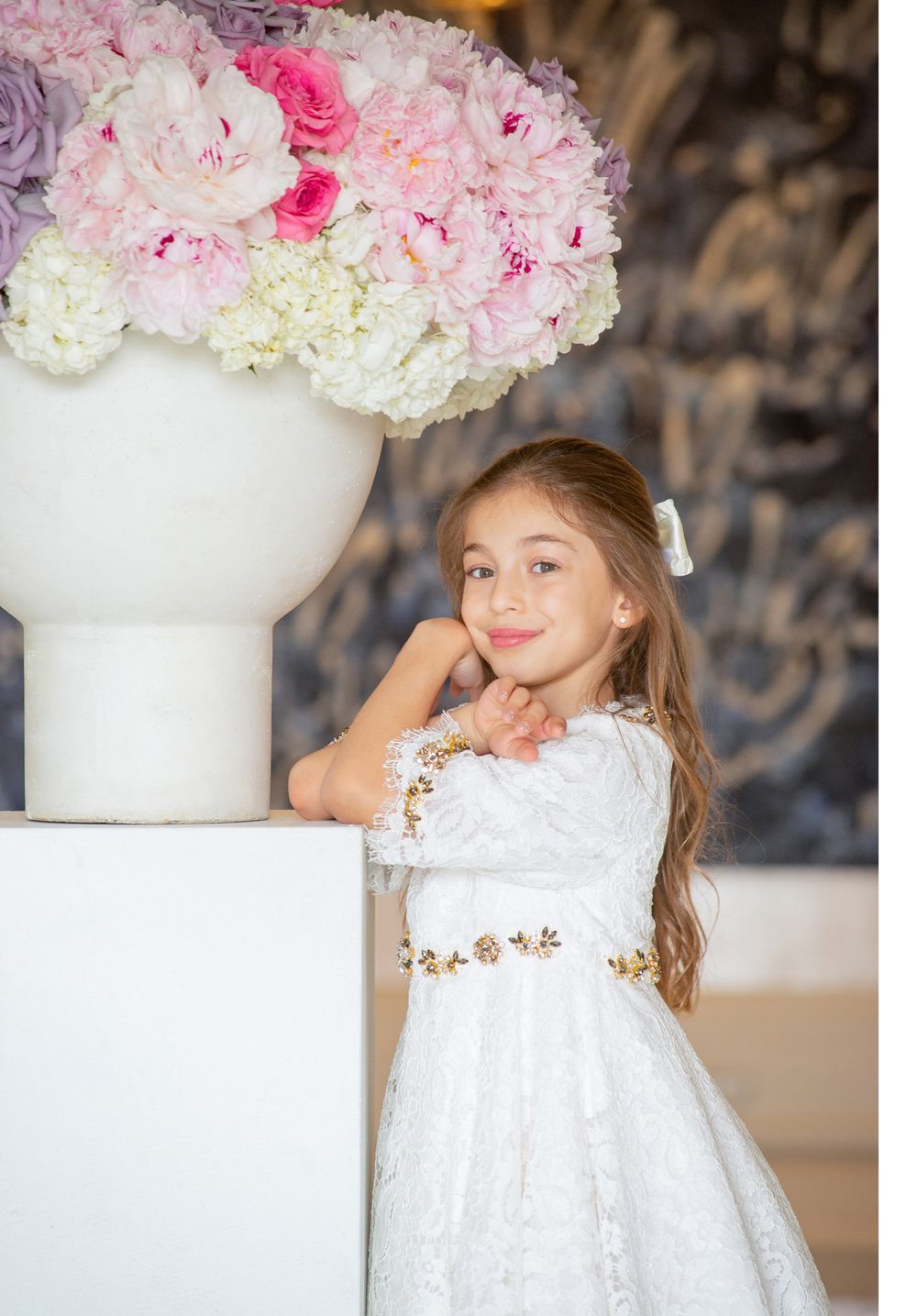 An elegant white floral arrangement with pink and purple blooms sits atop a white pedestal.