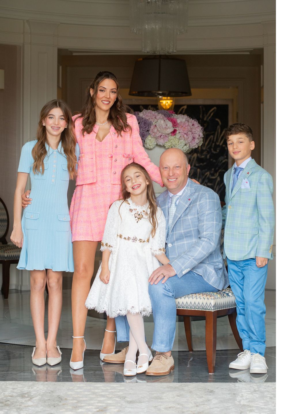 A family portrait featuring coordinated pastel outfits against an elegant interior setting.