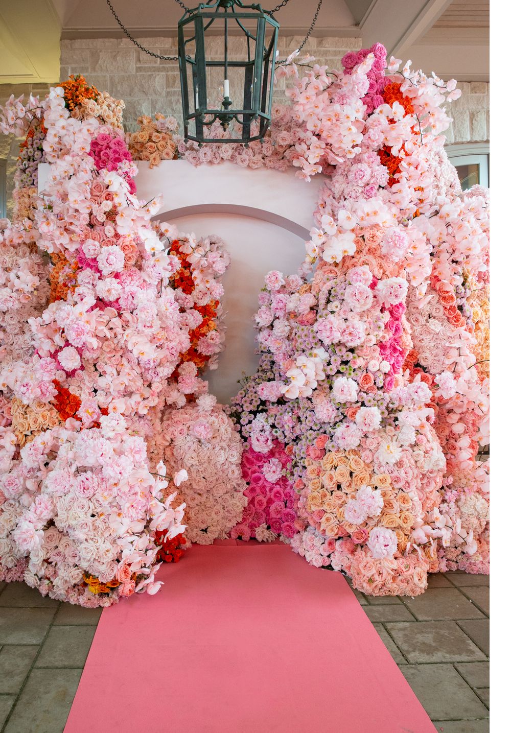 A stunning floral arch made of pink and coral flowers creates a romantic walkway with a pink carpet.
