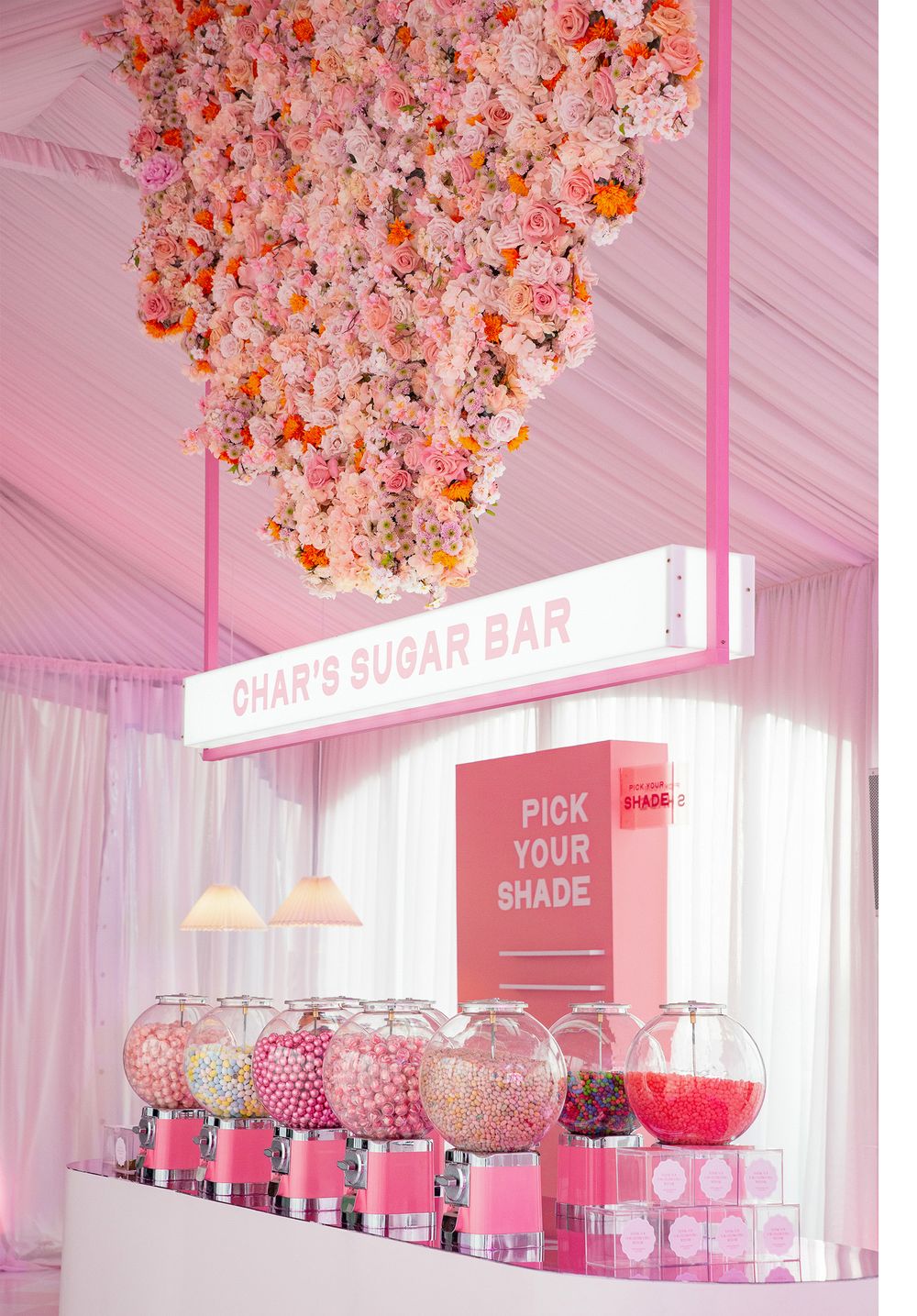 Pink sugar bar display with hanging floral installations and candy dispensers.