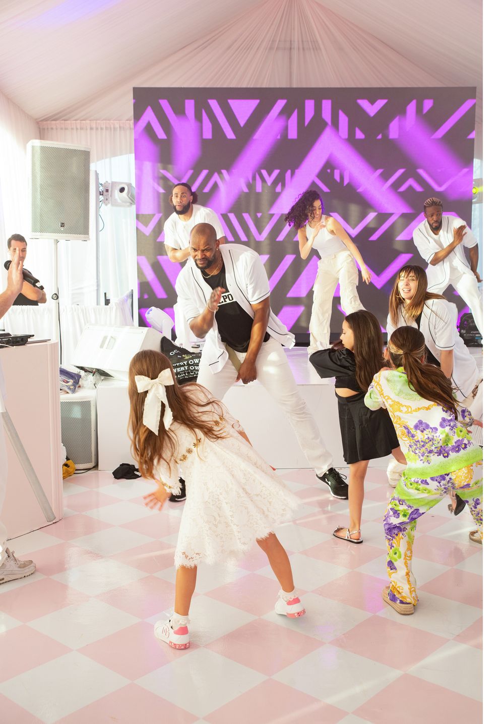 Dancers perform on a checkered pink and white floor with purple lighting effects in the background.