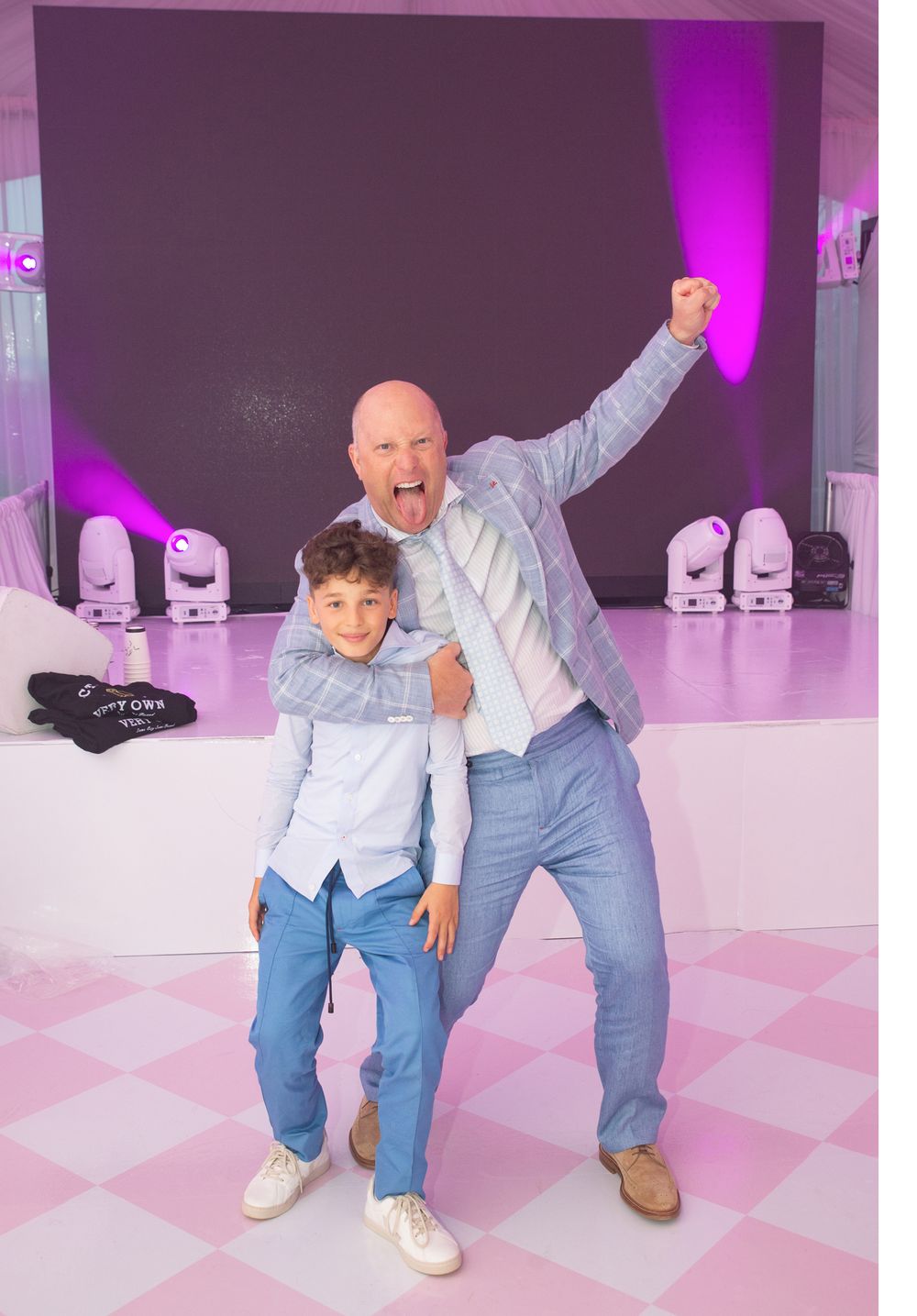 A joyful dance celebration on a pink and white checkered floor with purple stage lighting.