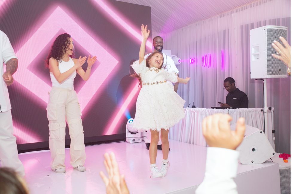 Energetic dancers move to the music in a white and pink illuminated party space.