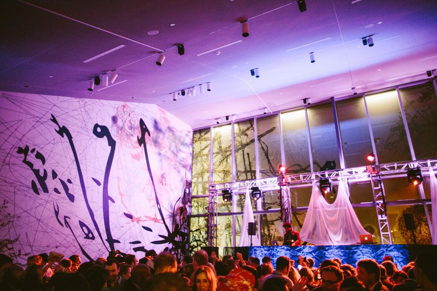 Concert stage with purple lighting features silhouetted performers and large white backdrop with artistic projections.
