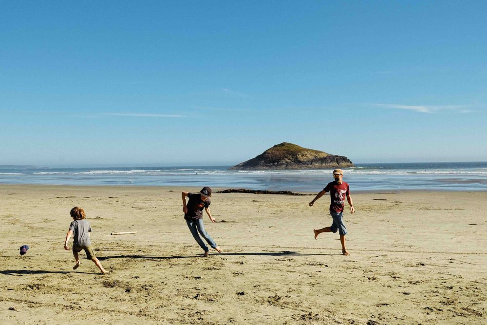 People playing and running on a beach with a distinctive hill island in the background.