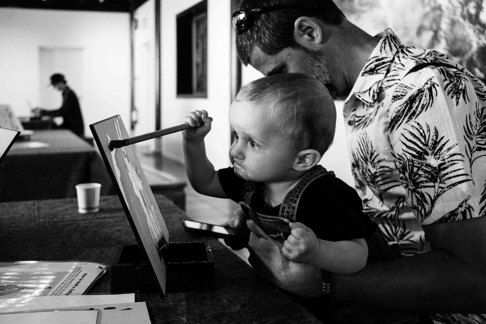 A black and white image showing someone helping a small child use a laptop computer.