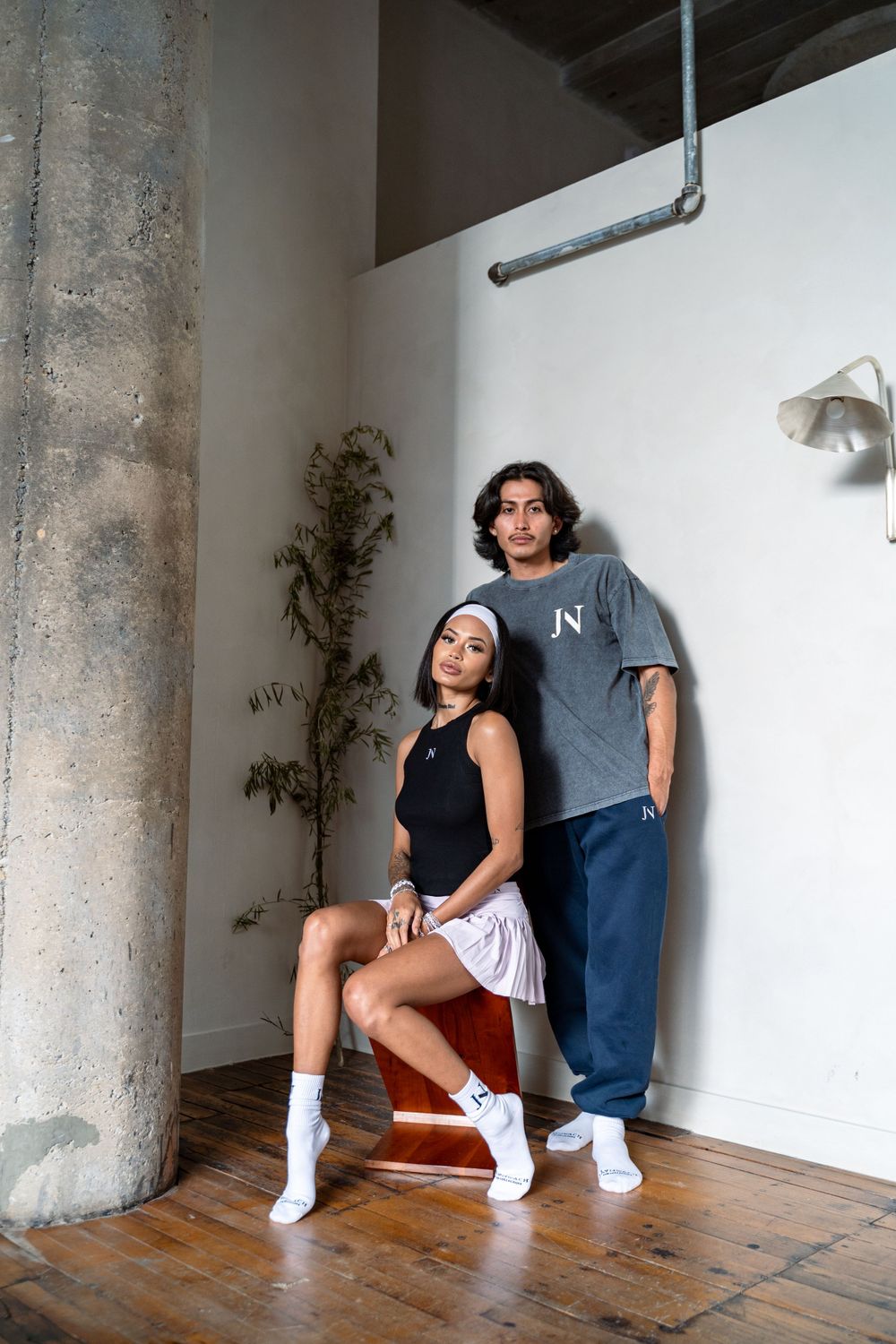 Two people in casual wear posing near concrete pillar in modern interior space.