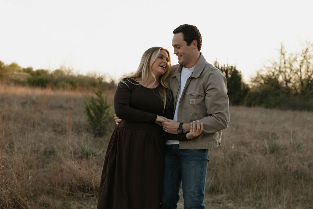 Happy pregnant couple smiling and embracing during a warm sunset maternity session.