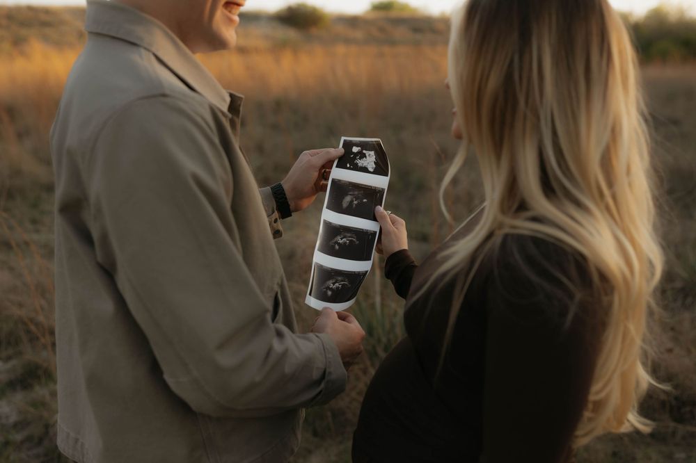 Expecting couple holding ultrasound photos together in a golden autumn field.
