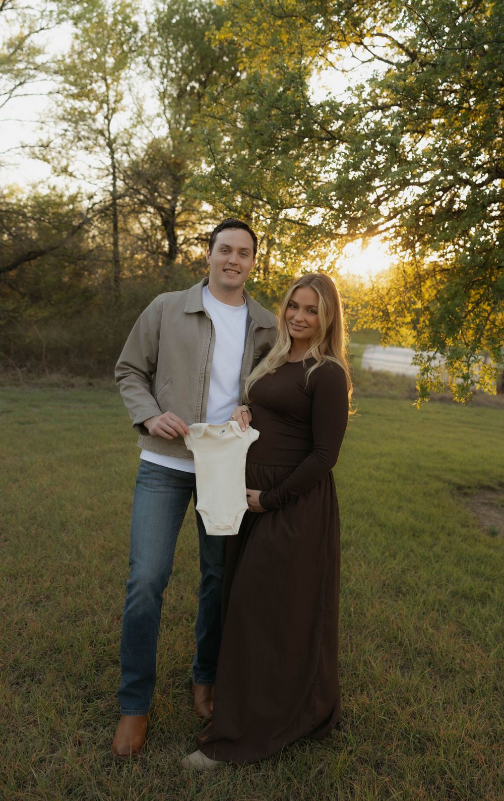 Couple holding a tiny baby onesie during a golden hour maternity photo session.