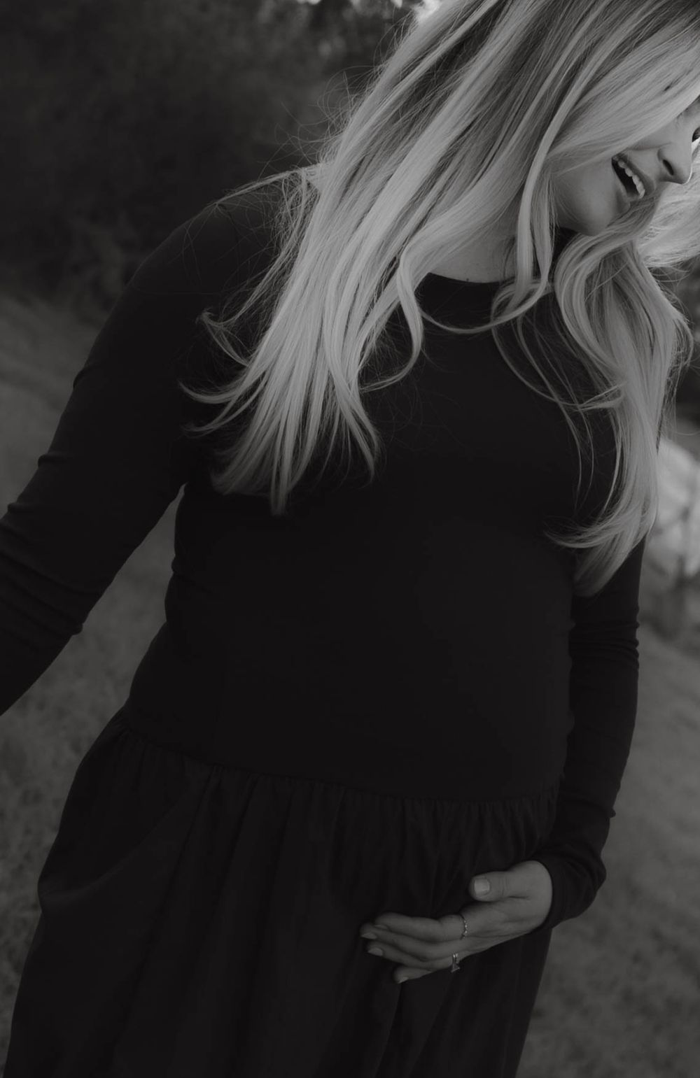 Close-up black and white photo of pregnant woman in dark dress gently cradling her baby bump.