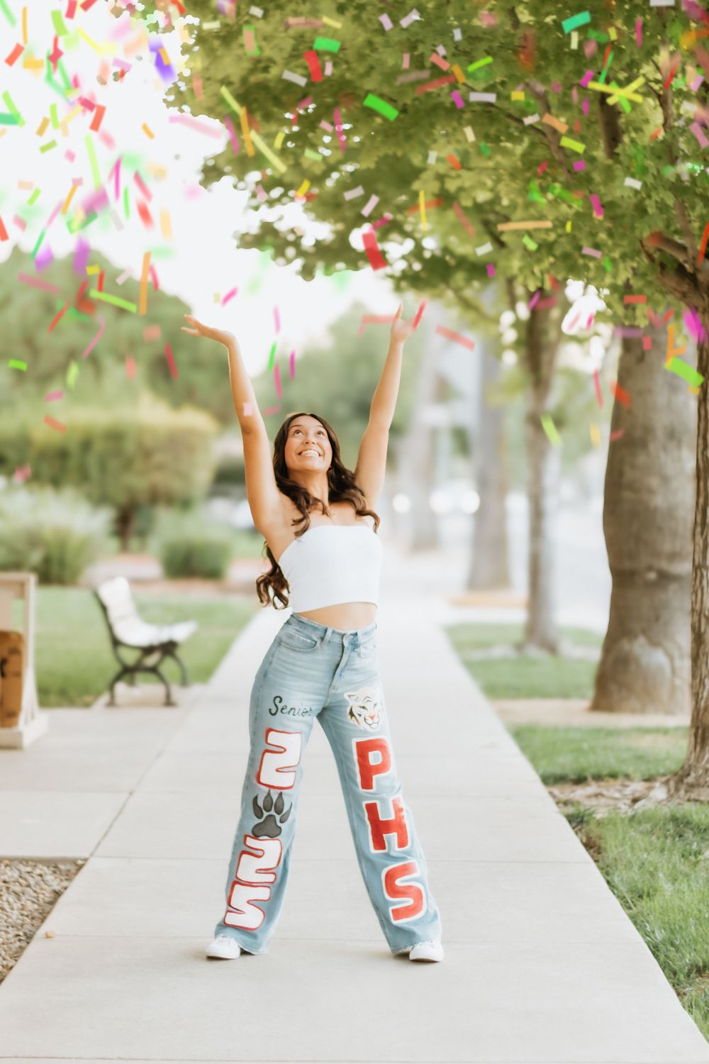 A celebratory moment with confetti flying under trees on a sidewalk during a graduation photoshoot.