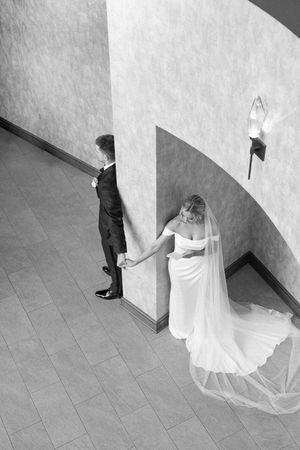 Black and white photo of bride and groom holding hands on a curved staircase, bride in flowing gown and veil.