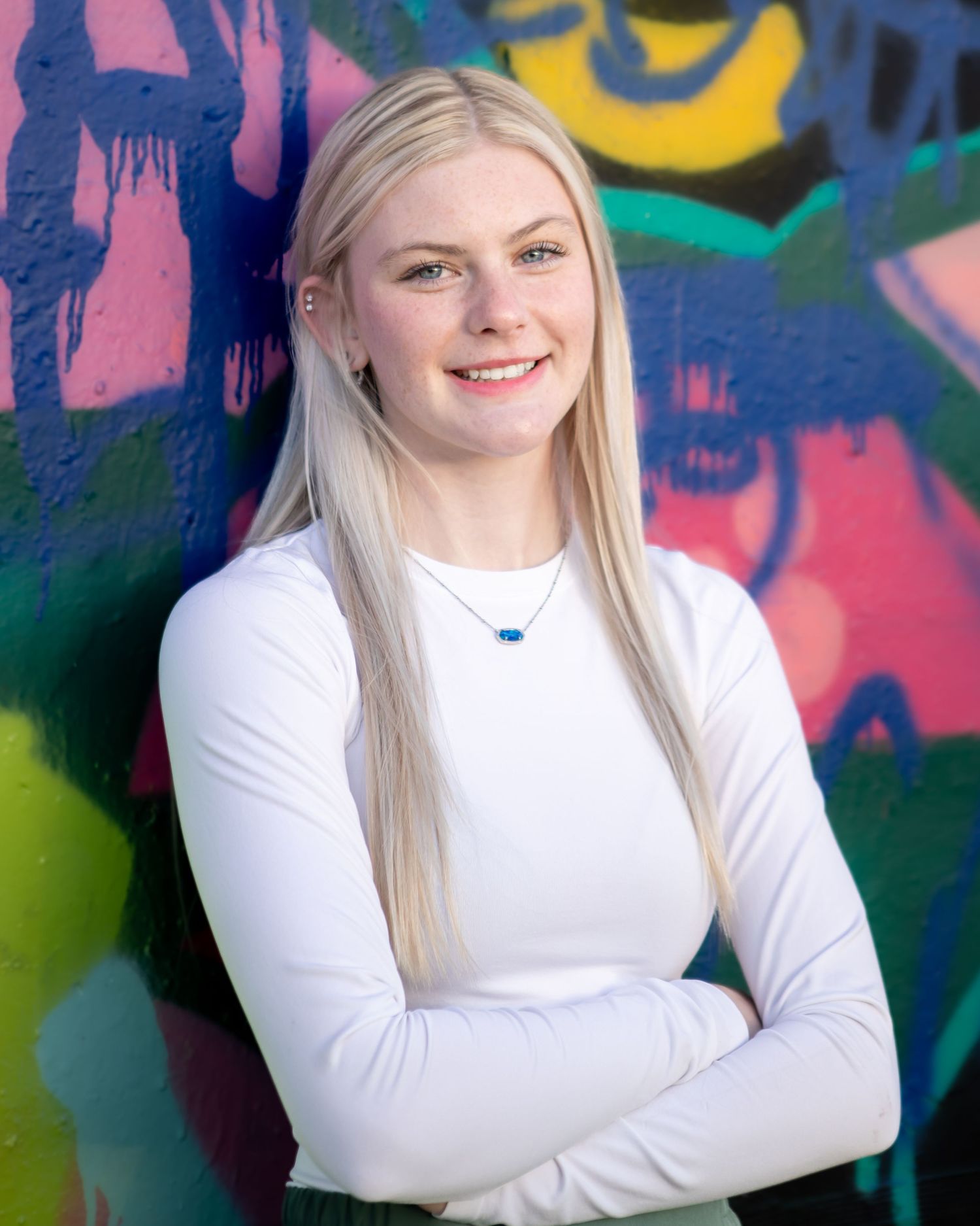 Person in white long sleeve top poses against colorful graffiti wall background.