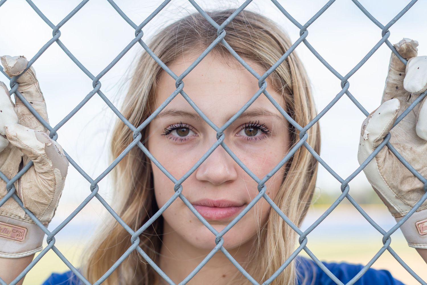 Student athlete poses behind chain link fence wearing a baseball glove.
