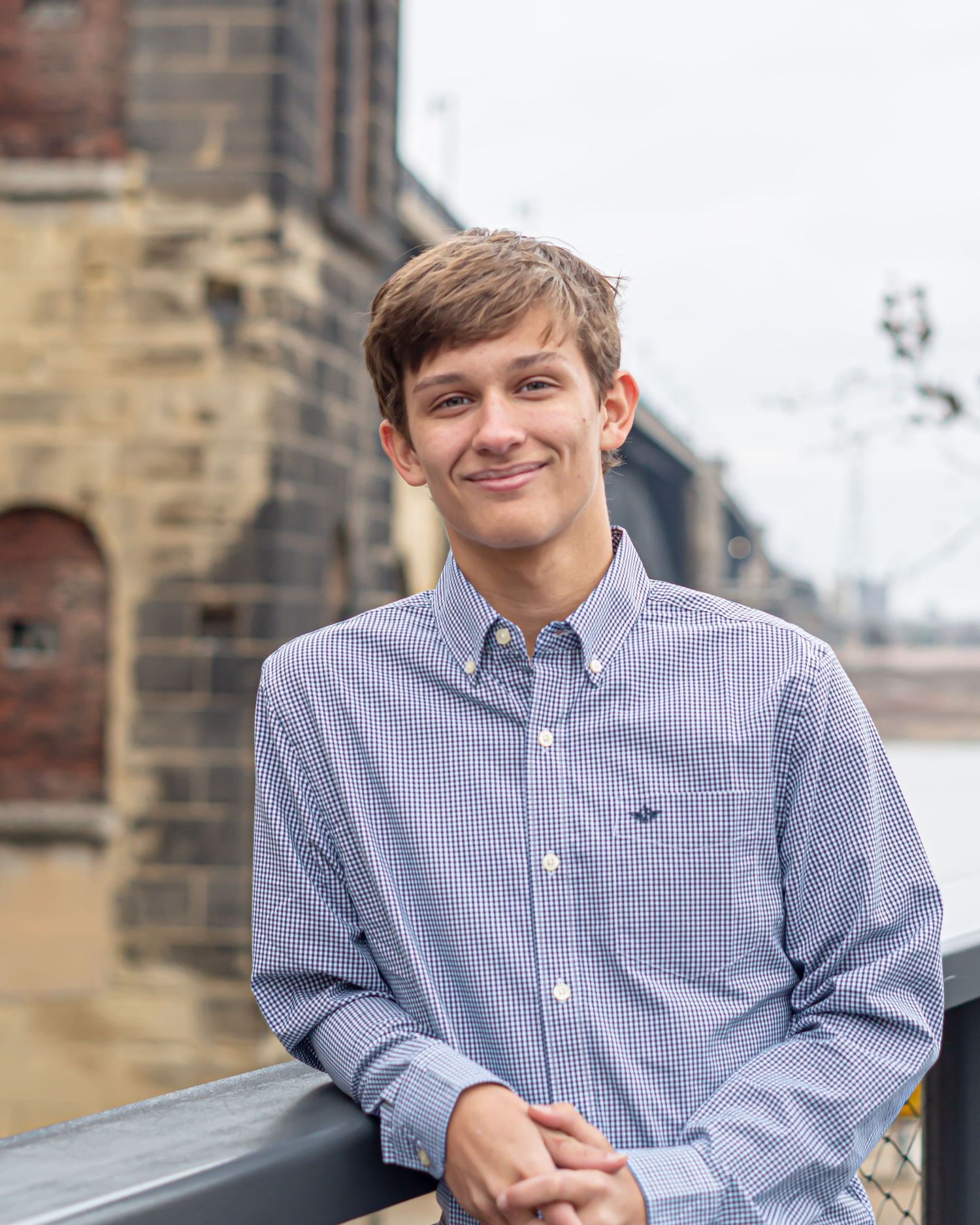 Student in blue gingham shirt smiling during outdoor portrait session.