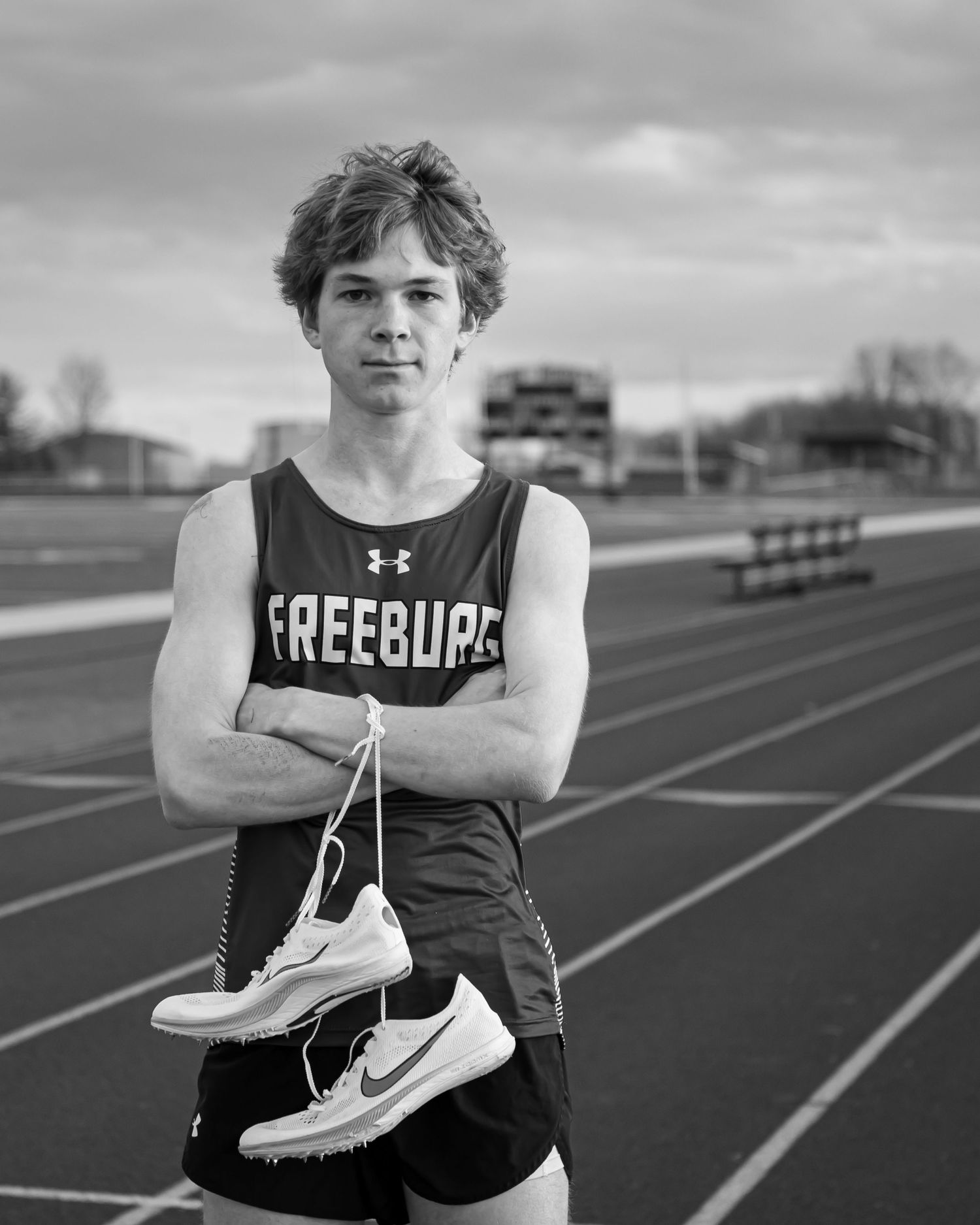 Track athlete in Freesquad uniform holds running shoes on outdoor track.