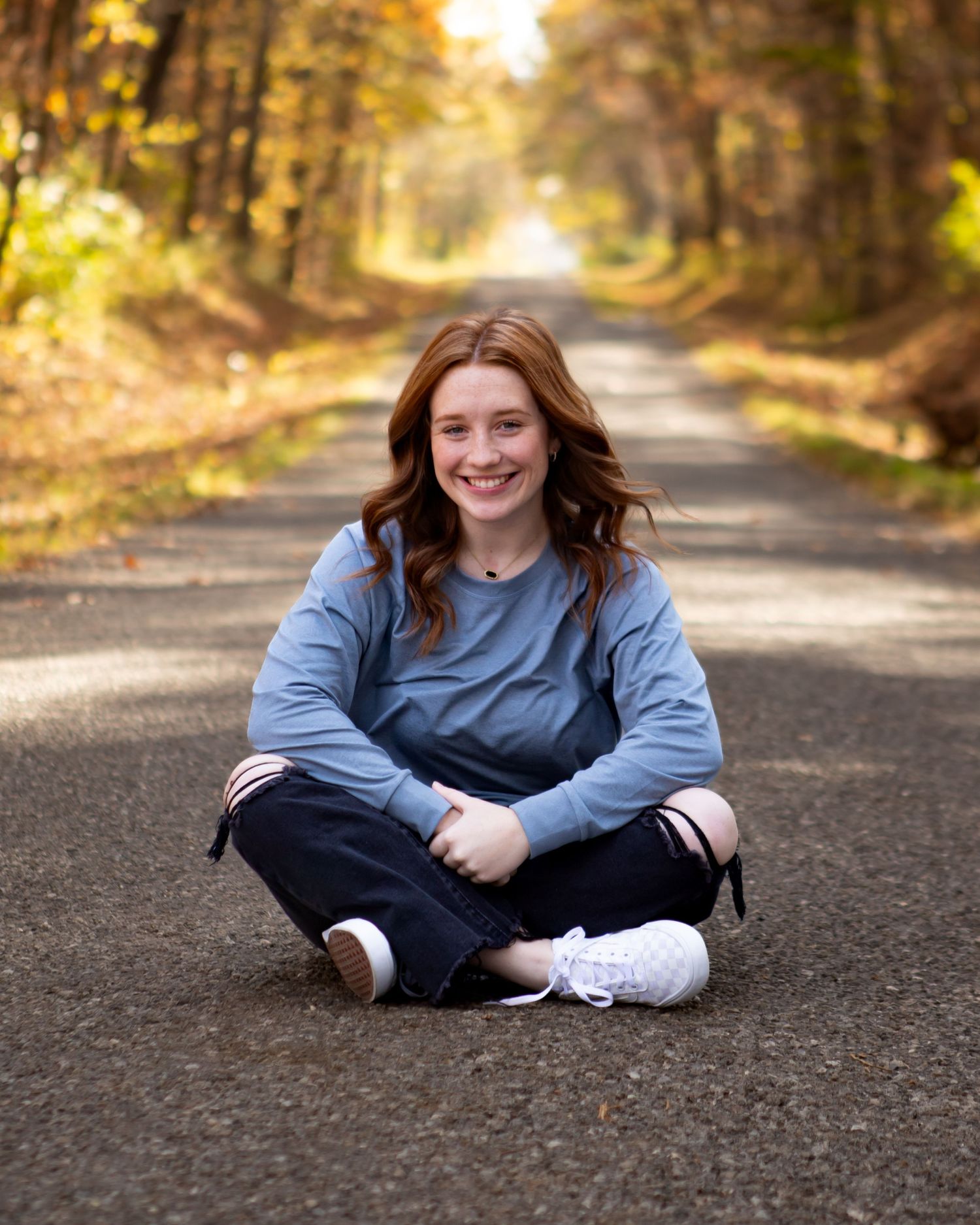 Autumn photo session on tree-lined path with golden sunlight filtering through leaves.
