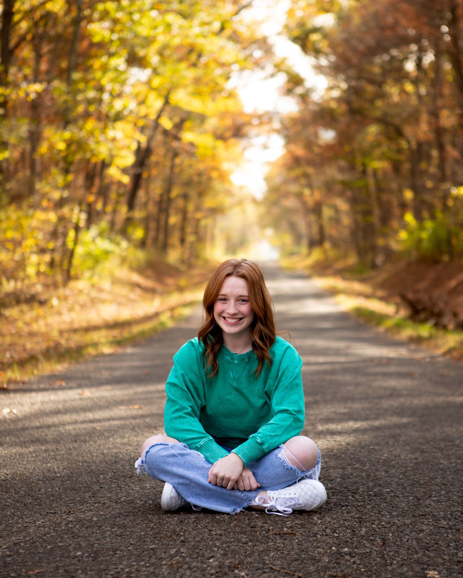 Casual autumn photoshoot on gravel road with green sweater and distressed jeans.