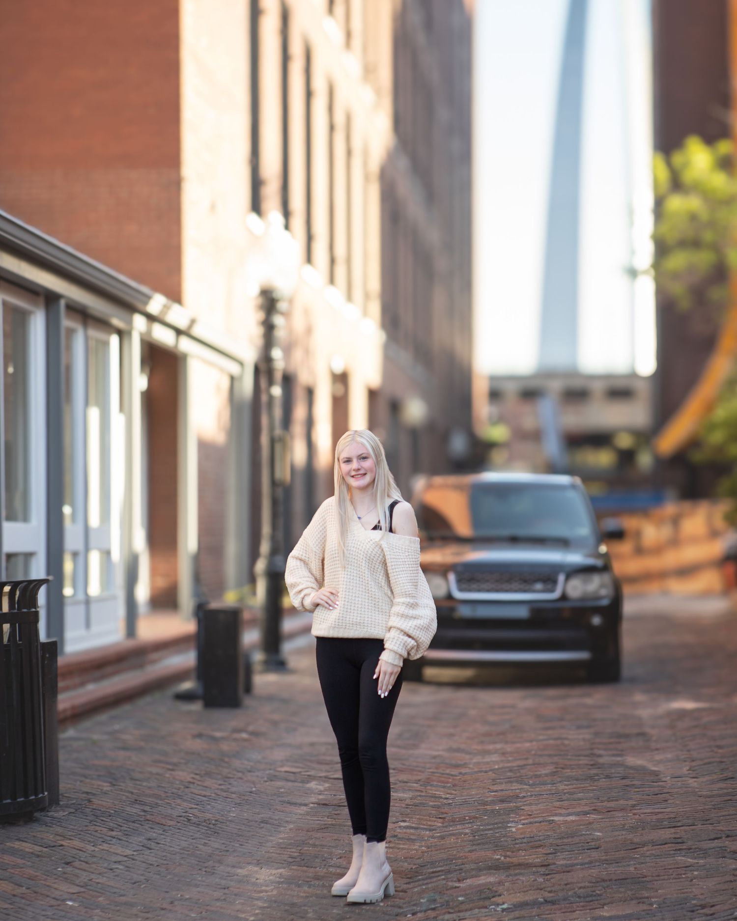 Figure walking along brick sidewalk in urban setting wearing light colored sweater.
