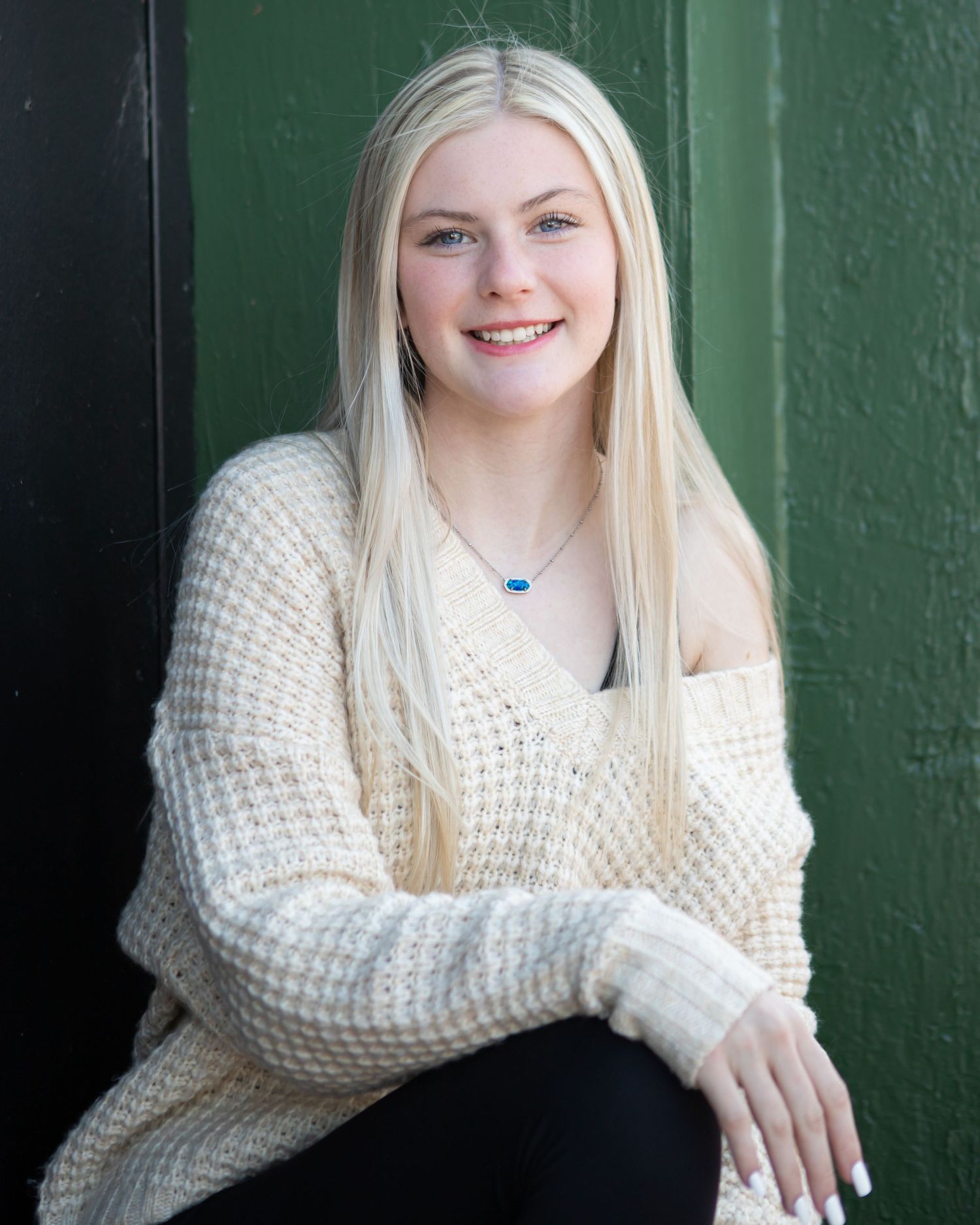 Cozy winter portrait against green wall wearing chunky knit cream sweater.