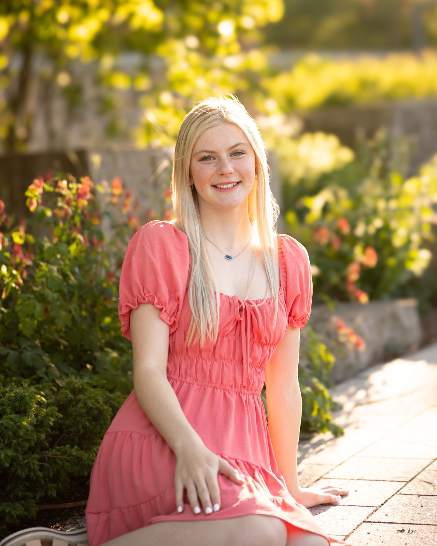Outdoor garden setting with coral pink dress amid blooming flowers and golden sunlight.