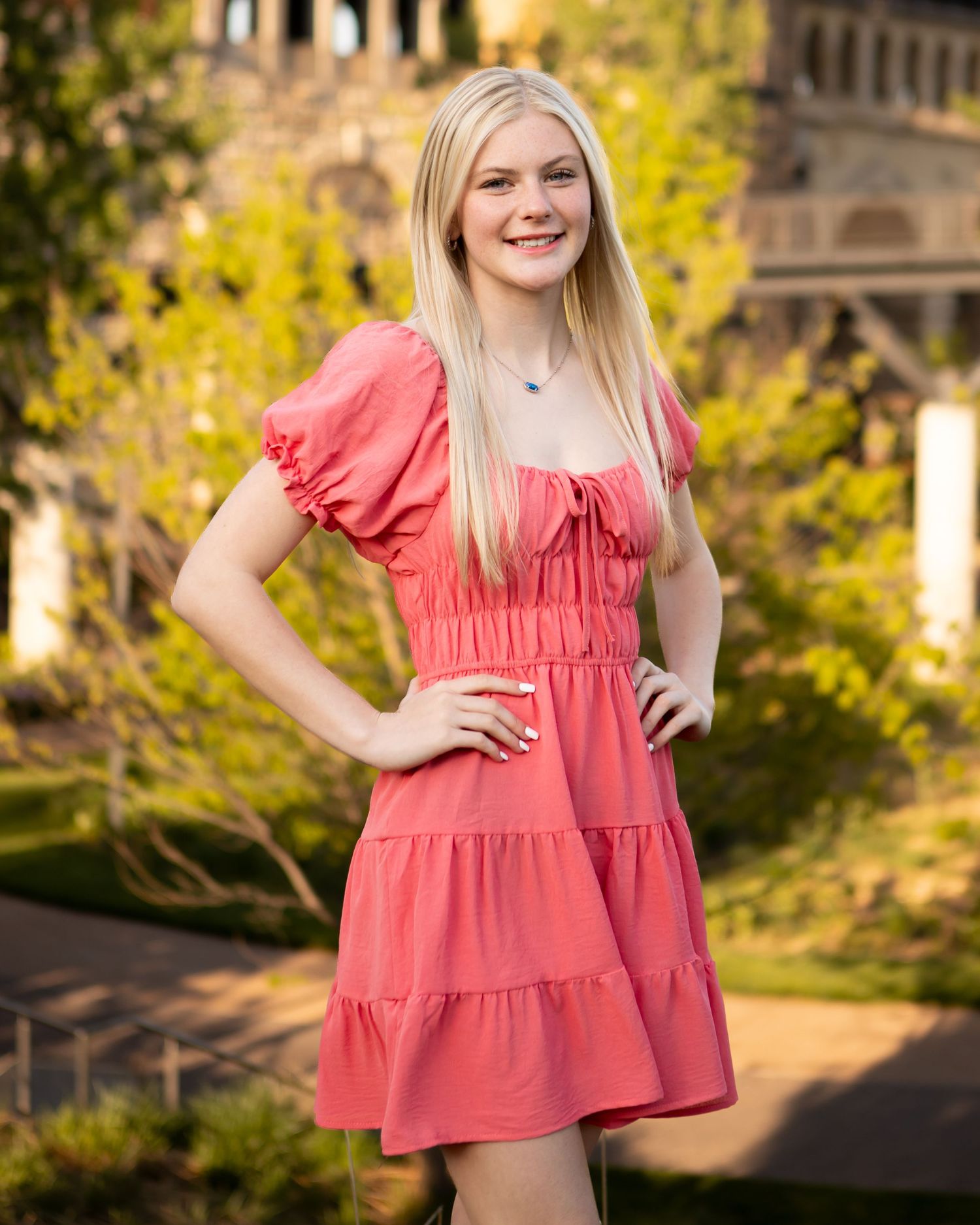 A coral ruffle dress is worn against a backdrop of autumn foliage in golden sunlight.