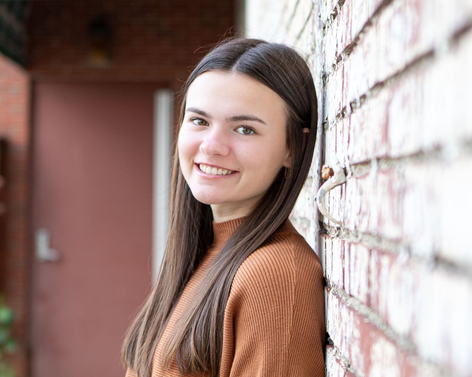 A brown sweater look is photographed against a textured brick wall backdrop.