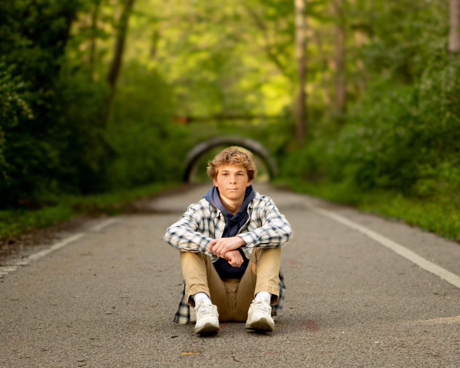Person sits cross-legged on paved path with stone tunnel in background.