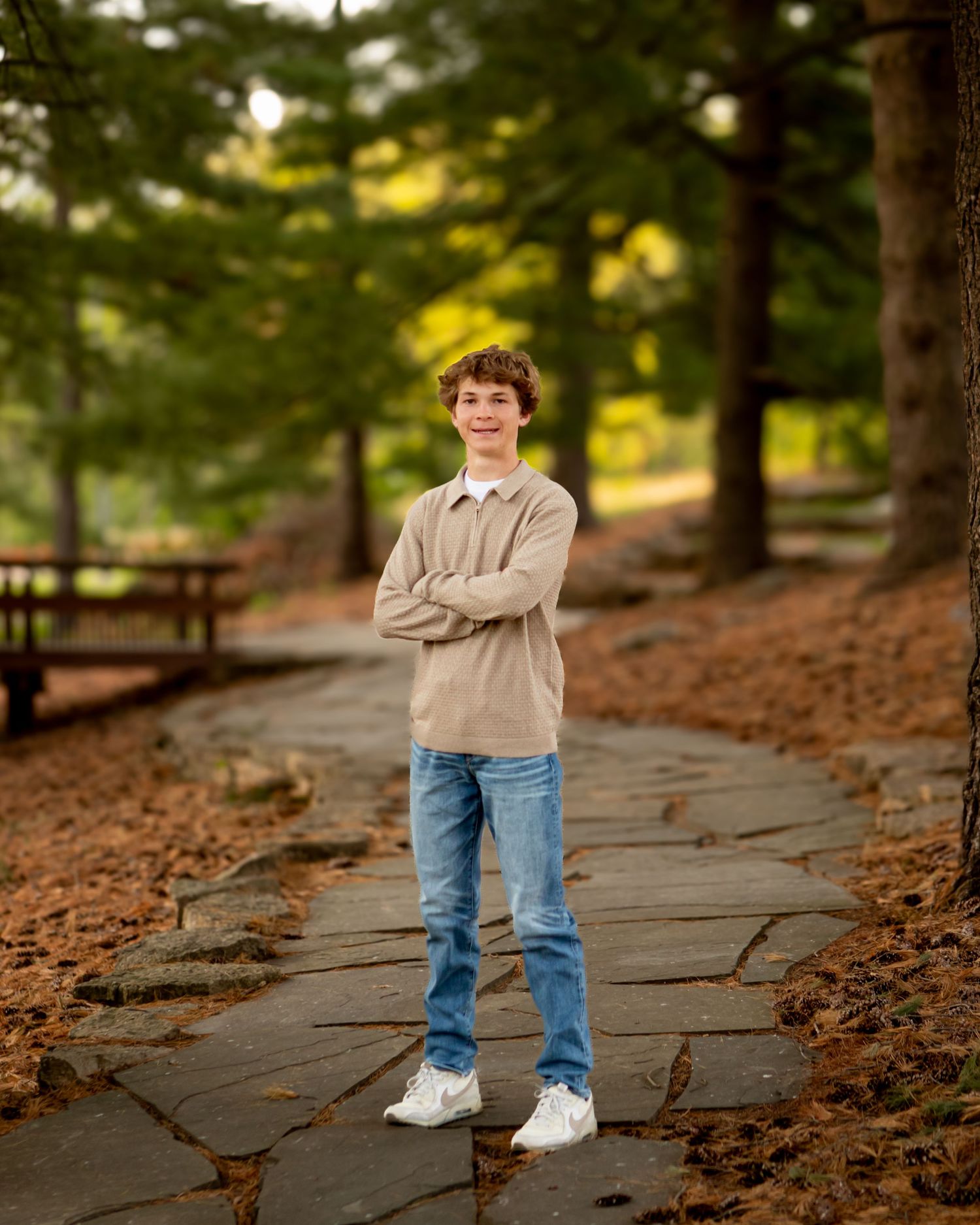 Person in beige sweater and jeans stands on stone path in autumn forest setting.